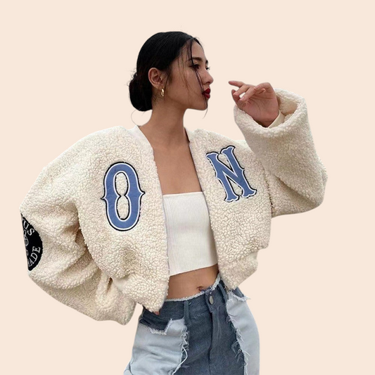 My Store apricot teddy varsity jacket with blue letter embroidery worn by a model on a beach