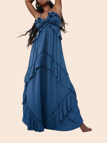 My Store blue ruffled tiered halter maxi dress with an open back, worn by a woman on a rocky beach at sunset.