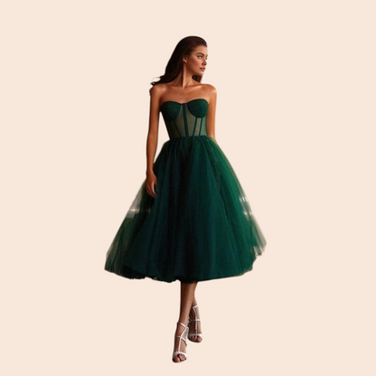 Model wearing a My Store emerald green strapless corset tulle midi dress with a voluminous skirt on a wooden deck