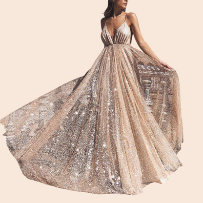 My Store Aurelia gold shimmer maxi gown with a deep plunging neckline and full skirt worn outdoors at a plaza.