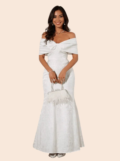 My Store white off-shoulder maxi dress with a statement bow bodice and flared hem worn by a smiling model.